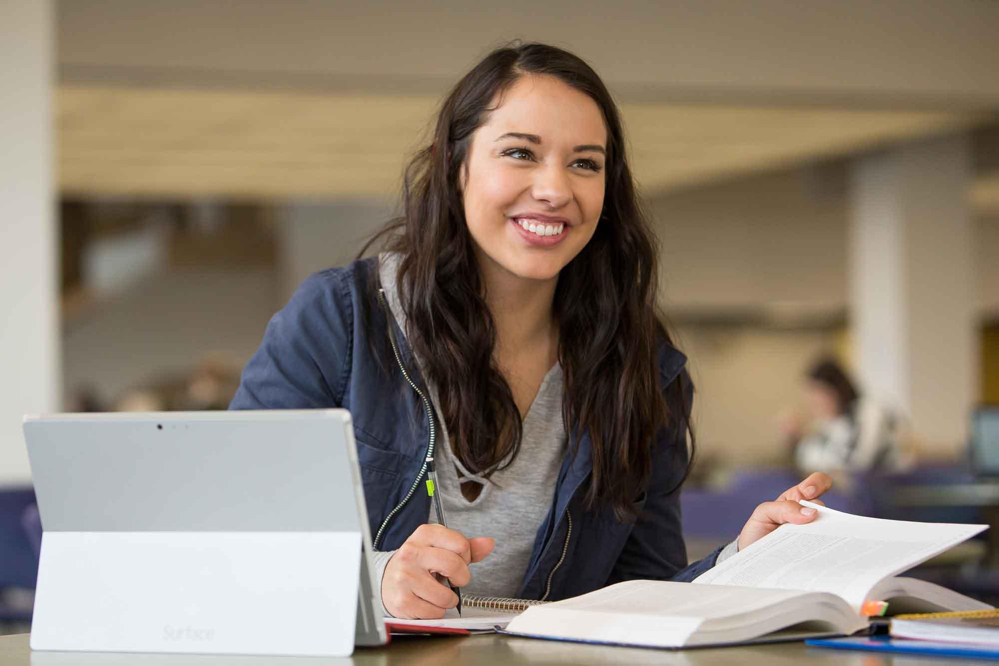 Transfer student sitting at work desk on UNC campus with a book an ipad.